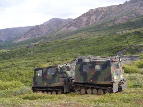 2003 Jeep TJ - Two camouflaged articulated tracked vehicles are parked in a grassy, mountainous landscape.