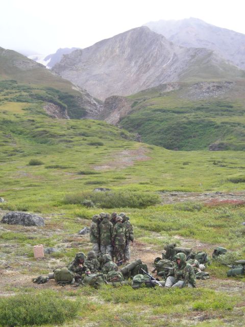 2003 Jeep TJ - Soldiers take a break in a remote, mountainous terrain, surrounded by green hills and rocky peaks.