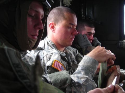 2003 Jeep TJ - Soldiers in camouflage uniforms are seen inside a vehicle, with one preparing to eat from a meal pouch.