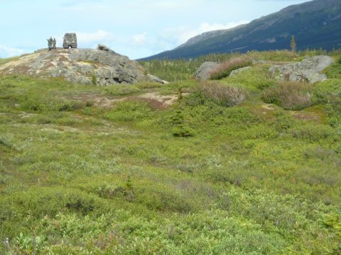 2003 Jeep TJ - Two individuals stand with a military vehicle on a rocky hill, overlooking a vast, green, and mountainous landscape.