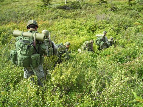 2003 Jeep TJ - A group of soldiers in camouflage gear navigate through thick green undergrowth, each carrying substantial backpacks.