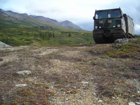 2003 Jeep TJ - A military all-terrain vehicle sits on a hillside under a cloudy sky, with a vast, green landscape stretching out behind it.