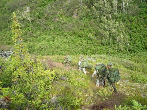 2003 Jeep TJ - A group of soldiers in camouflage gear trek through a natural landscape, carrying heavy packs.