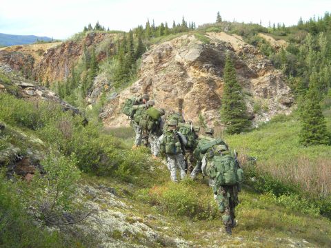 2003 Jeep TJ - A group of soldiers trek through a , natural landscape, their heavy packs indicating a challenging journey.