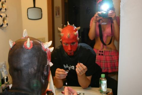 1995 Ford Probe - A person with a red mask and horns applies makeup in a bathroom mirror, with a reflection of another person holding a camera.