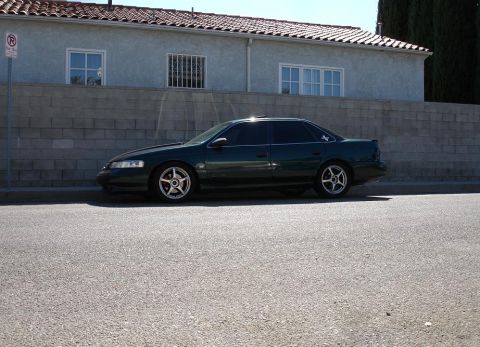 1993 Ford Taurus - A dark green sedan with aftermarket wheels is parked on the side of the road.