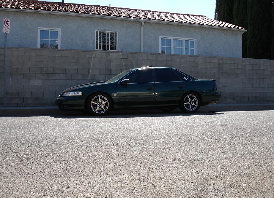 Dark green sedan parked on asphalt, side view. Aftermarket wheels with red brake calipers visible