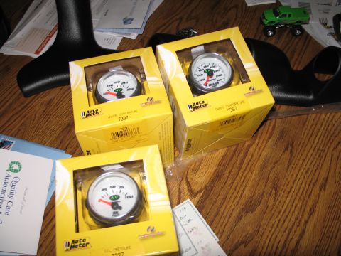 1995 Ford Bronco - Three new Auto Meter gauges are displayed on a wooden table, ready for installation in a vehicle.