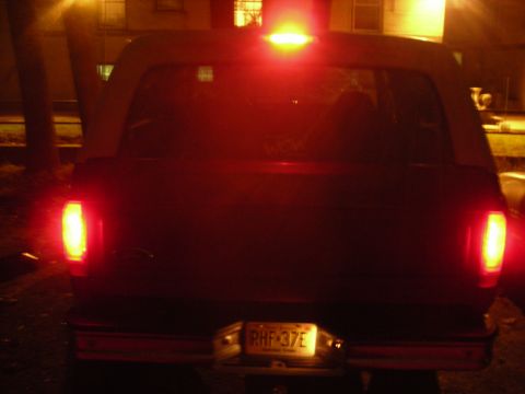 1995 Ford Bronco - The rear of a dark SUV is visible at night, with its brake lights and license plate illuminated.