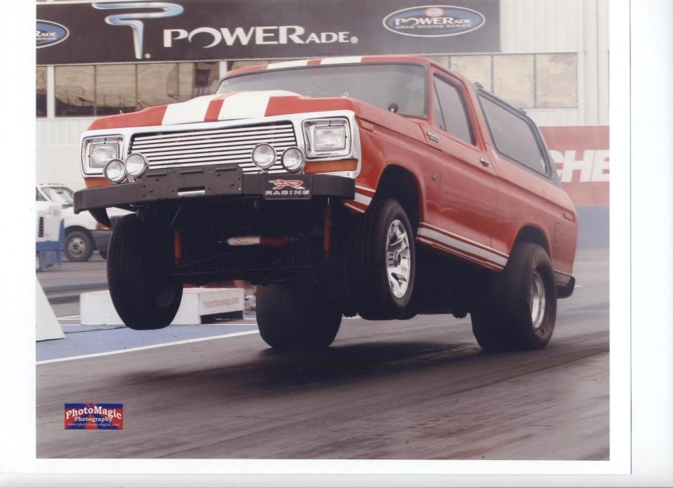 Red and white Ford Bronco doing a wheelie at a drag strip