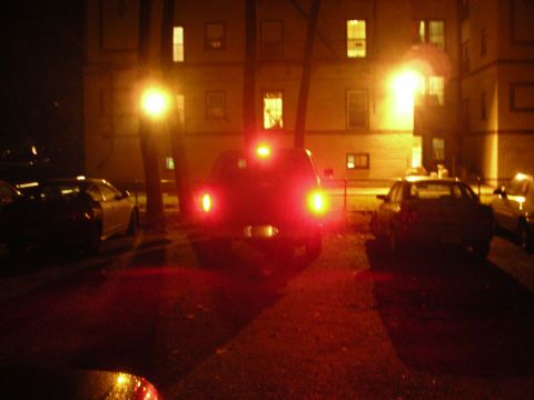 1995 Ford Bronco - The rear of an SUV is visible at night, with its brake lights on. Other vehicles are parked nearby.