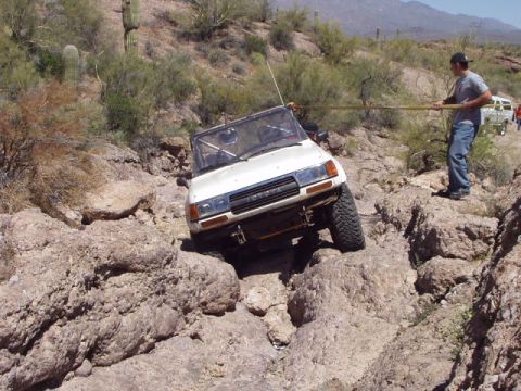 1993 Ford Bronco - A white off-road SUV navigates a challenging rocky path in a desert landscape, with a person assisting.
