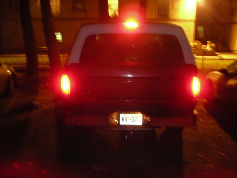 1995 Ford Bronco - The rear of a dark red SUV with a white roof is visible, with its taillights illuminated.