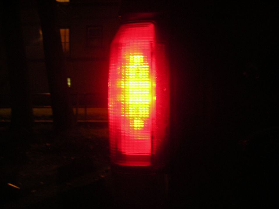 Red taillight with yellow bulb illuminated, dark background, Supermotors.net logo at bottom right