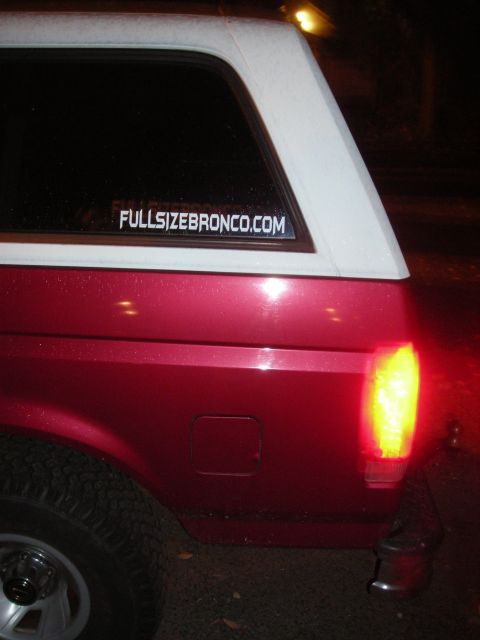 1995 Ford Bronco - Rear view of a red and white SUV, a sticker on the rear window and an illuminated taillight.