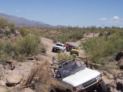 1993 Ford Bronco - Several off-road vehicles navigate a rocky desert trail, with one vehicle being towed.
