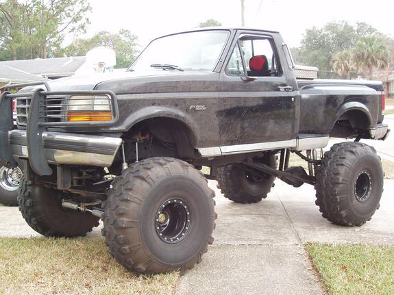 Lifted black pickup truck with large off-road tires and a brush guard. The truck appears to be a 1992 Ford F-150 or F-250
