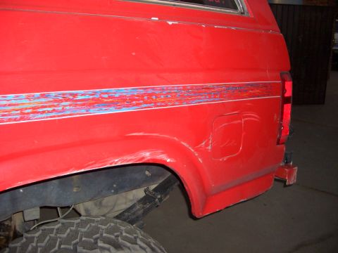 1985 Ford Bronco - Rear side view of a red SUV showing damage and a worn decal stripe.