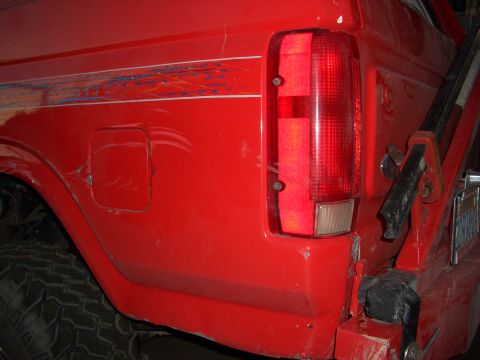 1985 Ford Bronco - Rear view of a red truck, showing the quarter panel, taillight, and a portion of the spare tire mount.
