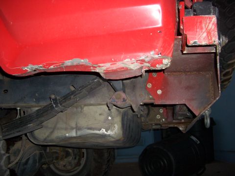 1985 Ford Bronco - The rear underside of a red vehicle shows rust damage and exposed suspension parts.