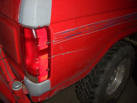 1985 Ford Bronco - Rear view of a red SUV showing its quarter panel, graphics, and tire.