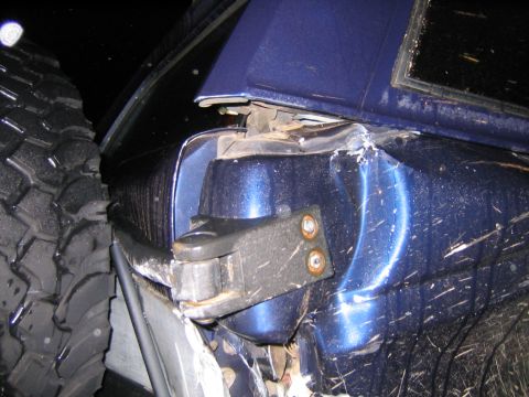 1994 Ford Bronco - The rear corner of a blue SUV shows significant damage, with a large tire pressed close to the body.