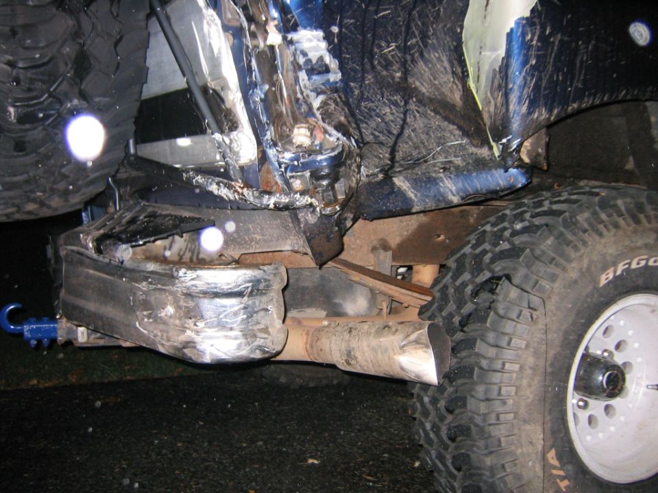 Wrecked front underside of lifted blue Bronco at night with crushed bumper and BFG tires