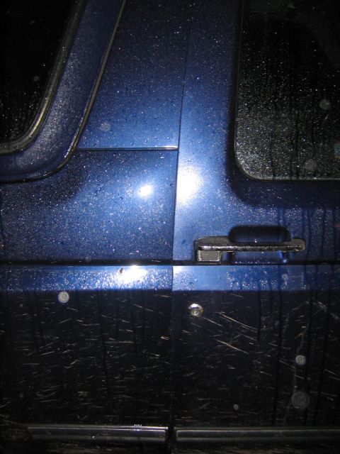1994 Ford Bronco - The side of a blue SUV is covered in water droplets and mud, obscuring its model year.