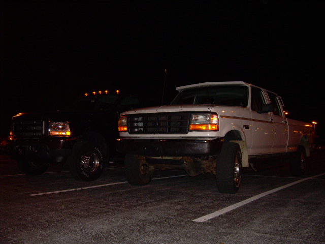 Dark and white lifted Ford trucks parked at night