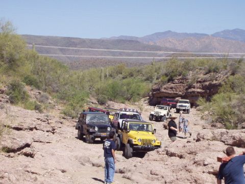 1993 Ford Bronco - A convoy of off-road vehicles, primarily Jeeps, traverses a desert terrain under a clear blue sky.