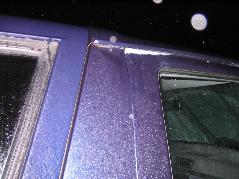 Close-up of buckled and torn purple B-pillar at the roof drip rail on a damaged truck at night