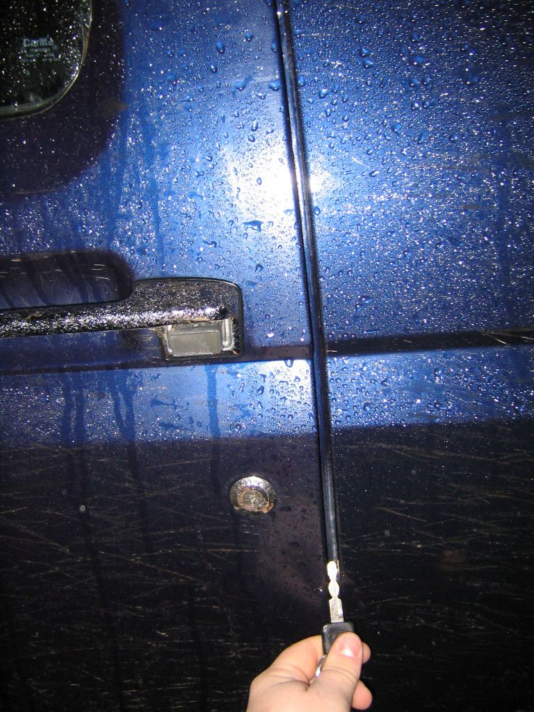 Hand holding key near wet dark blue vehicle door with chrome handle and lock