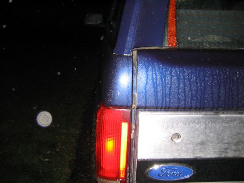 1994 Ford Bronco - The rear of a blue SUV is shown at night with water droplets on its surface.
