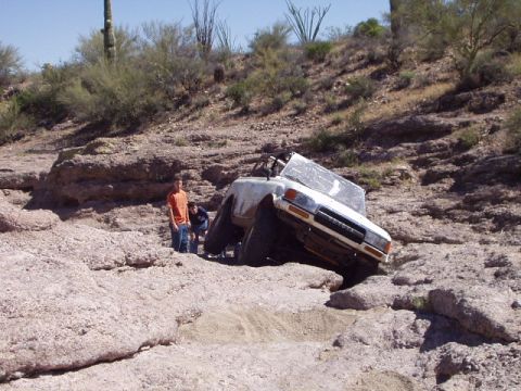 1993 Ford Bronco - A white 1993 Ford Bronco is stuck in a rocky desert landscape with two people standing nearby.