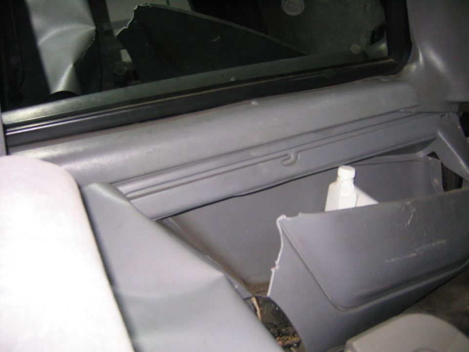 Damaged gray SUV interior side panel with broken storage pocket and shattered window glass
