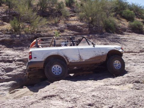 1993 Ford Bronco - White off-road SUV with roll cage navigating a rocky, off-road trail.