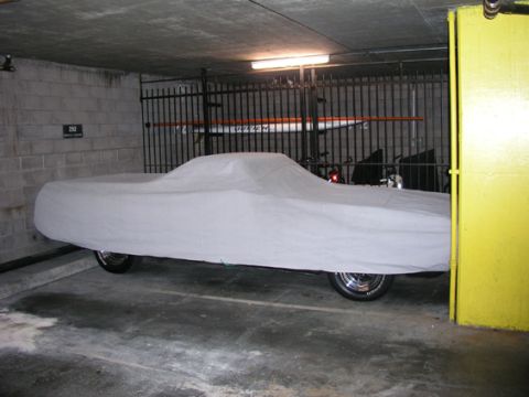 1972 Ford Ranchero - A vehicle is covered by a sheet in a dimly lit garage, with a yellow pillar to the right.