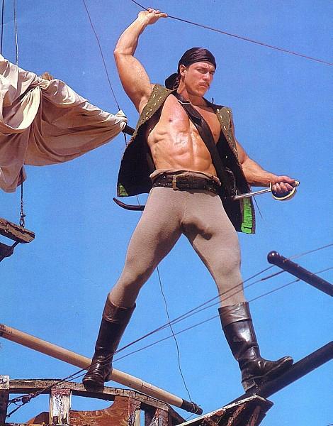 1986 Ford Bronco - A man dressed as a pirate stands on wooden beams against a blue sky, holding a sword and a rope.