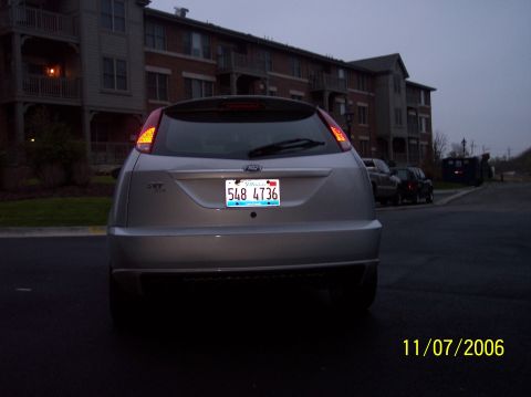 2003 Ford Focus - This silver hatchback, identified as a 2003 Ford Focus, is parked in front of apartment buildings.