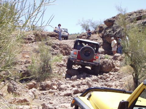 1993 Ford Bronco - A Jeep Wrangler tackles a challenging rocky trail, with other vehicles and onlookers present.