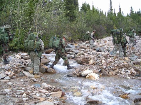 2003 Jeep TJ - A group of soldiers navigates a shallow stream in a mountainous, forested environment.