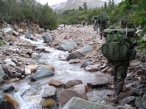 2003 Jeep TJ - A group of soldiers navigates a stream bed in a , natural landscape.