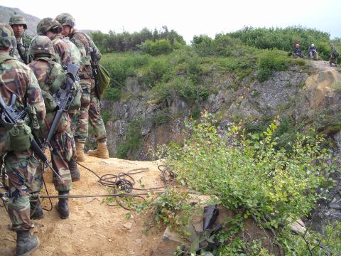 2003 Jeep TJ - A group of soldiers equipped with rifles stand near a cliff edge, with ropes and equipment visible on the ground.
