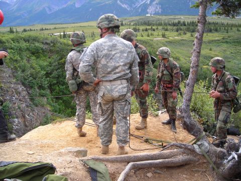 2003 Jeep TJ - Soldiers in camouflage gear stand on a ridge, with ropes and harnesses set up for rappelling down a steep incline.