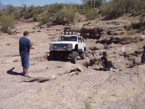 1993 Ford Bronco - A white Jeep Cherokee navigates a rocky off-road course under a clear sky.