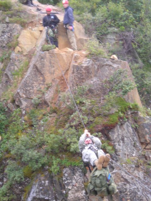 2003 Jeep TJ - People are rappelling down a steep, rocky incline with trees and vegetation.