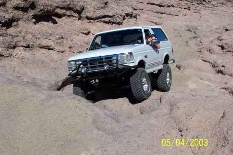 1993 Ford Bronco - A white Ford Bronco is shown off-roading on a rocky, desert-like landscape.