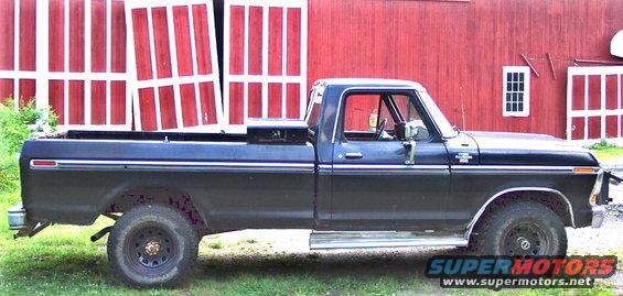 Side view of a black 1979 Ford F-250 pickup truck parked in front of a red barn