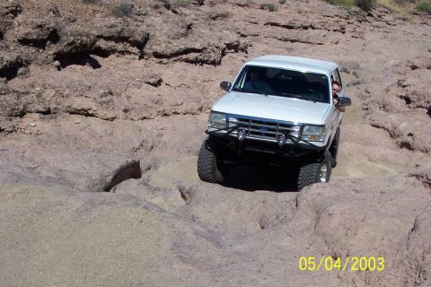 1993 Ford Bronco - A white 1993 Ford Bronco tackles a challenging rocky terrain on an off-road trail.