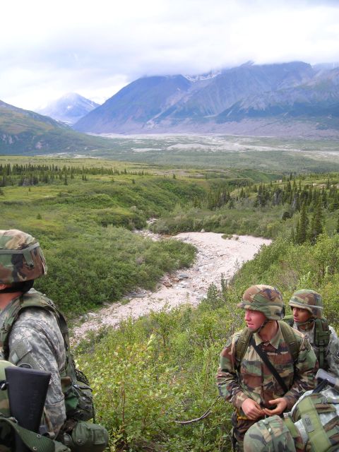 2003 Jeep TJ - Soldiers survey a vast valley and riverbed, with mountains in the background under a cloudy sky.